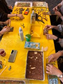 hands around a table with yellow covering making mosaics